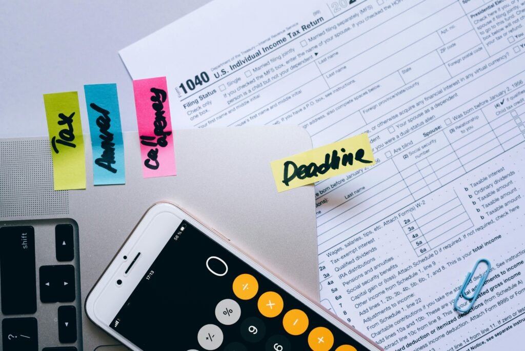 pexels-photo-8962519-8962519 Office desk flat lay showing tax documents, calculator app on smartphone, sticky notes, and paperclips.